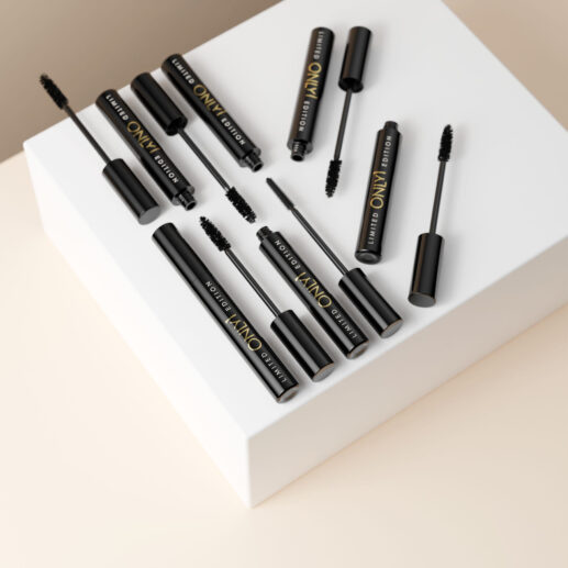 Multiple black mascara tubes and wands arranged on a white geometric pedestal against a beige background.