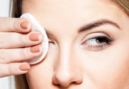 Woman gently pressing a cotton pad to her eye, demonstrating how to remove waterproof mascara without rubbing or irritation.