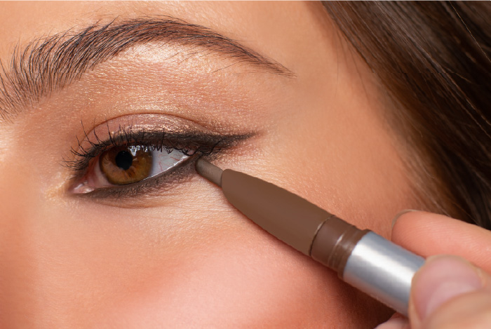 Close-up of a person applying eyeliner with brown eyes