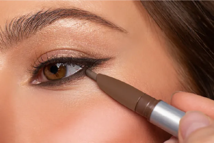 Close-up of a person applying eyeliner with brown eyes